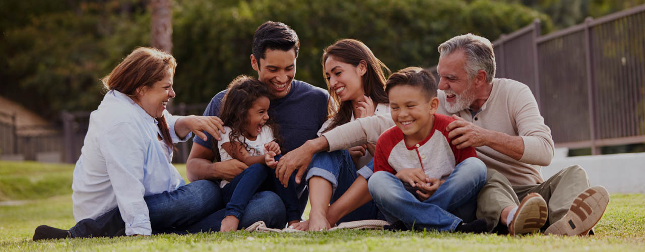 Happy three generation Hispanic family sitting on the grass toge
